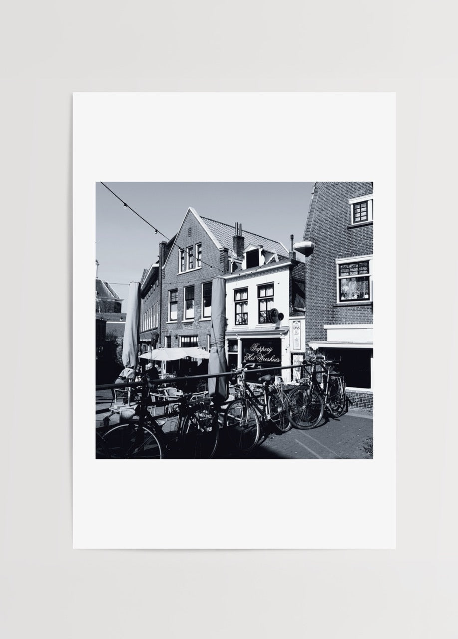 Merve Kurt’un Amsterdam’da çektiği siyah-beyaz fotoğraf, bisikletler ve tarihi kafe detaylarını ölümsüzleştiren poster baskı.