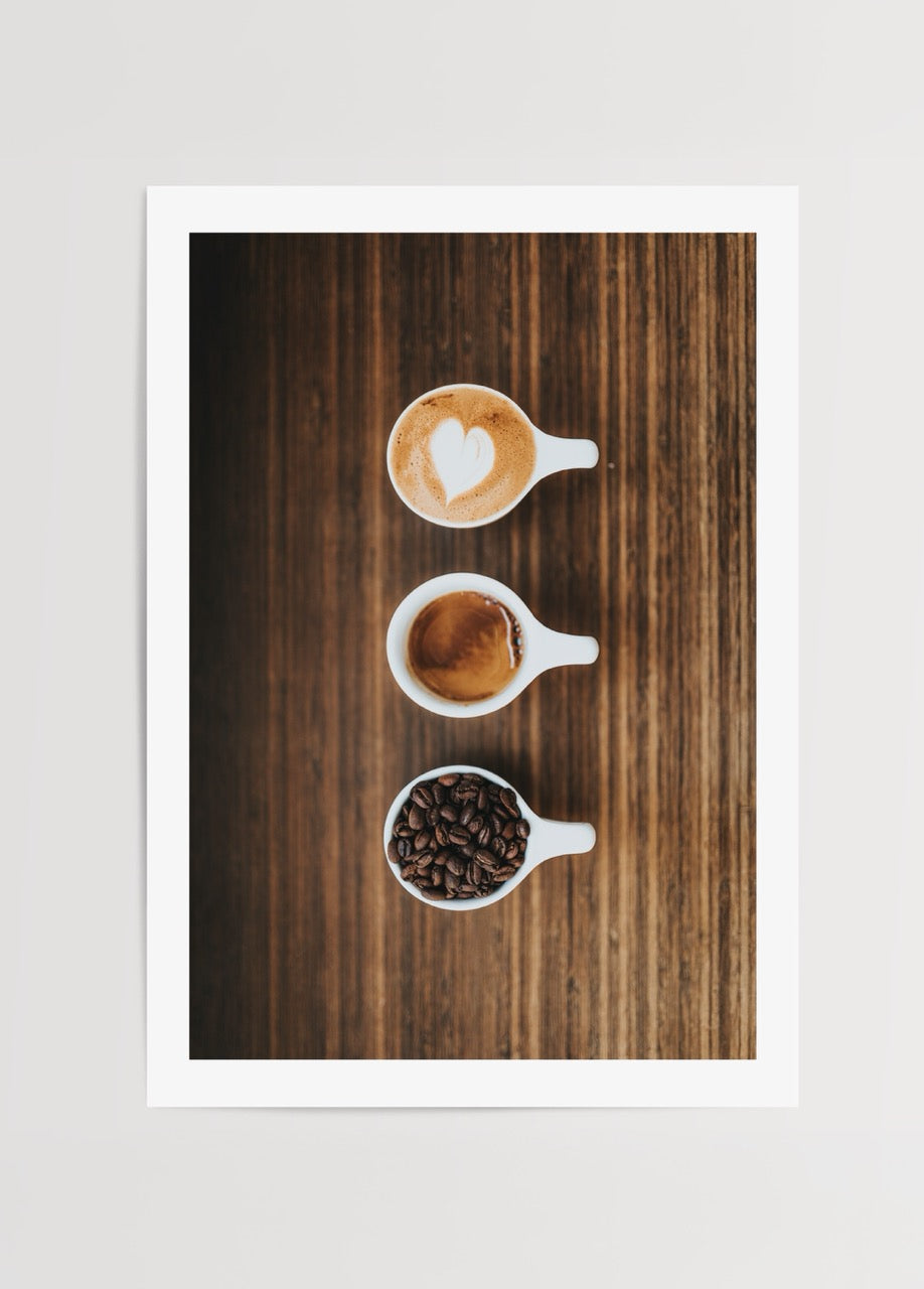 Ahşap yüzey üzerinde çekirdek, espresso ve sütlü kahveyi gösteren üç beyaz fincanlı minimalist kahve posteri
