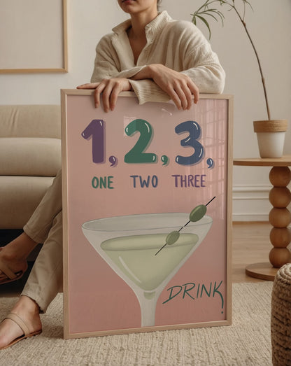 Özge Özcan One Two Three posteri; martini bardağı ve “1, 2, 3, Drink” yazılı pastel illüstrasyon.