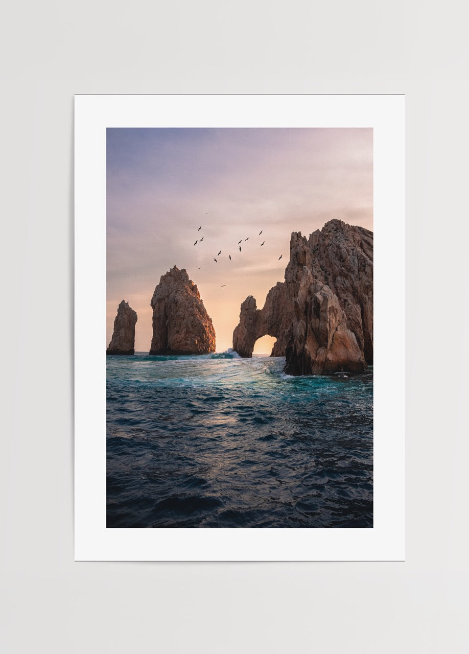 Gün batımında deniz üzerinde kaya kemerleri ve uçan kuşlar, doğa ve seyahat temalı poster.